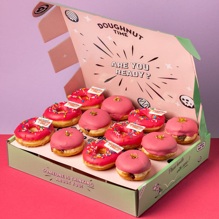 Edle grüne Geschenkbox mit zwölf roten Donuts die Hälfte mit einem "Frauentag" Topper, die Hälfte mit Blattgold verziert.
